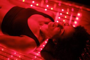 A multiracial woman on an LED light bed, receiving red light therapy.