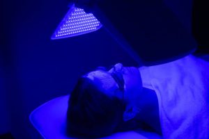 Young woman having blue LED light facial therapy treatment in beauty salon. Beauty and wellness concept